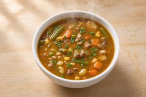 Bowl of homemade vegetable beef soup at Izzy’s, with beef, green beans, carrots, corn, peas, and beans in a rich broth.